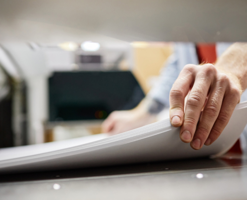 Close up of man putting stack of paper in printing machine at publishing shop, copy space
